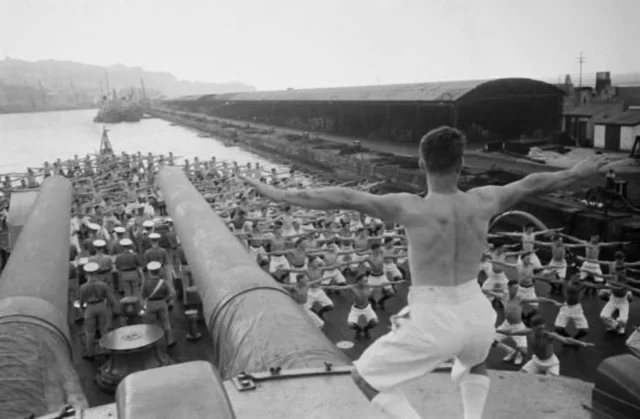 A Physical Training Instructor leads sailors through exercises aboard the battleship HMS Resolution while berthed at Gibraltar’s South Mole in October 1940 during WWII.

The instructor has taken position atop one of the ship’s 15-inch gun turrets, part of the battleship’s formidable main armament, as the crew maintains fitness and readiness during wartime service.

#gibraltar #wwii #ww2 #history #fitness

📸 Kenneth Busuttil